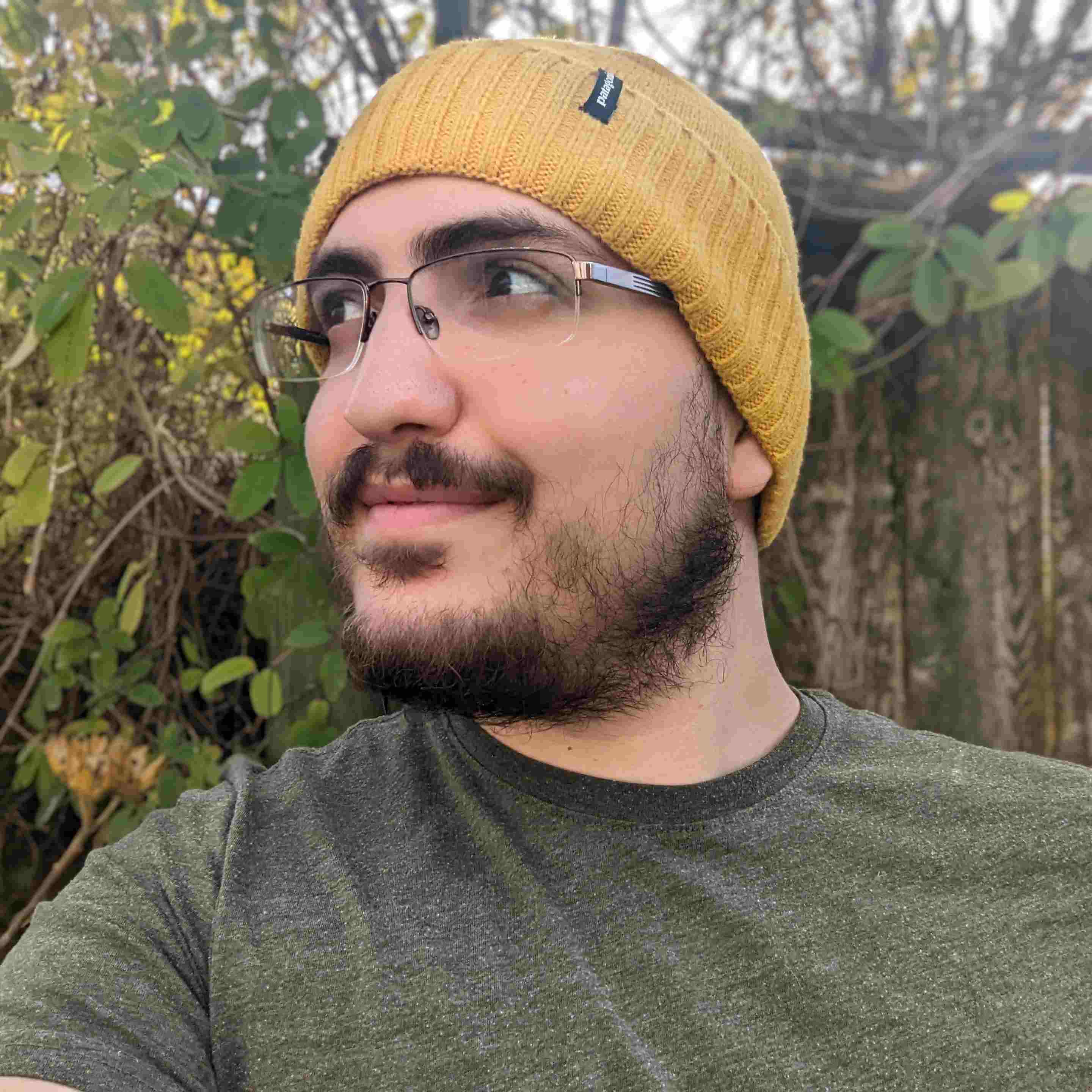 A picture of Kaan, wearing a beanie, in front of some shrubbery.
